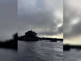 A moody shot of a house on a rocky outcrop, surrounded by water and clouds, creating an atmospheric scene.
