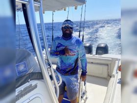 A smiling crew member gives a thumbs up aboard a fishing boat, showcasing the excitement of a day on the ocean.