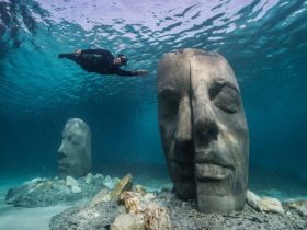 A diver explores stunning underwater sculptures, creating a captivating scene in crystal-clear waters — a unique experience for diving enthusiasts.