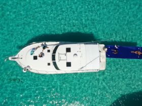 Aerial view of a group enjoying a day on the water, with some sunbathing on a floating mat beside the boat in stunning turquoise waters.