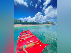 A group of friends relaxes on a floating mat in crystal-clear waters, enjoying a sunny day at the beach — the perfect setting for fun and relaxation.