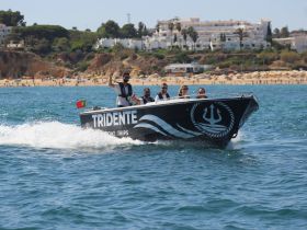 A lively group enjoys a boat trip on the water, with a beautiful beach backdrop — perfect for summer adventures and fun outings.