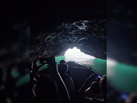 A group of adventurers captures the moment as their boat navigates through a cave, revealing a stunning view of turquoise waters beyond — a thrilling experience for nature lovers.