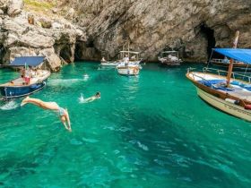 A vibrant scene of swimmers diving into crystal-clear waters surrounded by boats, showcasing the perfect summer getaway in a stunning coastal setting.
