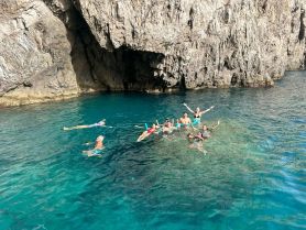 A lively group enjoys swimming in crystal-clear waters near a rocky cave, capturing the essence of adventure and fun in the sun.