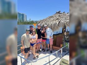 A lively group of friends enjoys a sunny day on a pontoon boat, celebrating together with drinks and fun in the water.