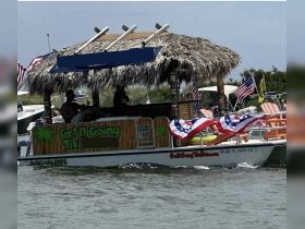 A vibrant tiki boat named 'Get It Going Tiki' cruises through the water, showcasing a festive atmosphere with flags and colorful seating — perfect for fun outings on the water.
