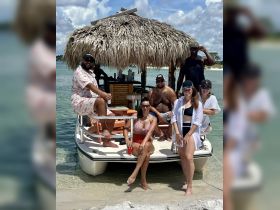 A lively group enjoys a fun day on a pontoon boat, soaking up the sun and sipping cocktails in a beautiful beach setting.