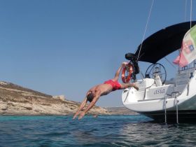 A man dives off the back of a sailboat into crystal-clear waters, capturing the essence of summer fun and adventure on the water.