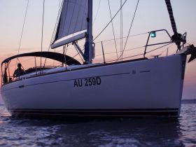 A sleek sailboat glides through the water at sunset, showcasing its elegant design and tranquil surroundings — perfect for sailing enthusiasts.