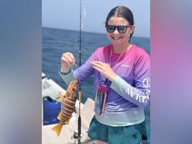 A young girl proudly holds up her catch while fishing on a boat, showcasing the joy of a successful fishing trip at sea.