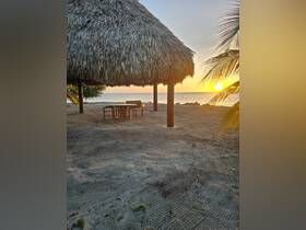 A serene beach scene featuring a thatched roof structure at sunset, perfect for relaxation and enjoying the coastal view.