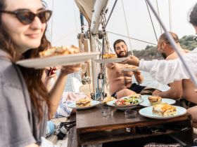 A lively group enjoys a delicious meal aboard a sailboat, sharing plates and laughter — perfect for memorable dining experiences on the water.