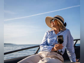 A woman enjoys a refreshing cocktail while relaxing on a boat under a clear blue sky — a perfect moment for leisure and enjoyment on the water.