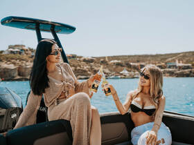 Two friends enjoy drinks on a boat, celebrating under the sun — perfect for summer outings and boat parties.