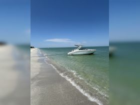 A sleek speedboat is anchored just off the sandy beach, showcasing a perfect day on the water under a clear blue sky.