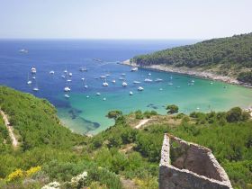 A stunning aerial view of a serene harbor filled with sailboats, surrounded by lush greenery and crystal-clear waters — an idyllic destination for sailing enthusiasts.