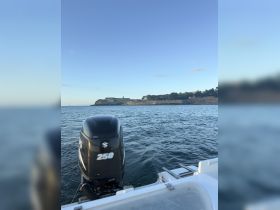 A clear view of a boat's motor with a scenic backdrop of a coastal landscape, showcasing the vessel in motion on the water.