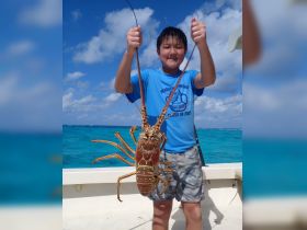 A young boy proudly holds up a large lobster caught during a fishing trip, showcasing the excitement of marine life encounters on the water.