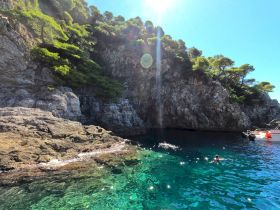 Swimmers enjoy the crystal-clear waters near a stunning rocky coastline, perfect for a refreshing dip during a boating adventure.