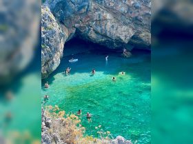 A lively group enjoys swimming in the crystal-clear waters of a cave, surrounded by stunning rock formations — a perfect spot for adventure and relaxation.