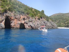 A scenic view of a boat navigating near rocky caves along the coastline, showcasing the beauty of the landscape and the adventure of exploring hidden gems on the water.