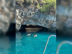Two swimmers explore a stunning cave entrance in crystal-clear waters, showcasing an adventurous day on the water.