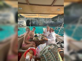 A cheerful group enjoys a delicious meal aboard a sailboat, surrounded by stunning turquoise waters — perfect for a memorable sailing experience.