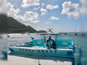 A group enjoys a sunny day aboard a vibrant boat, surrounded by stunning coastal scenery and anchored vessels — perfect for a memorable day on the water.