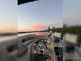 A view of the helm and seating area inside a Bentley boat, with a scenic sunset reflecting on the water in the background, perfect for relaxing cruises.