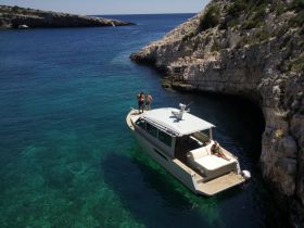 A group enjoys a sunny day on a boat anchored in a picturesque cove, perfect for swimming and relaxation in crystal-clear waters.