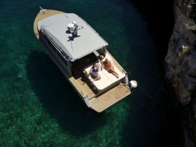 Aerial view of a couple relaxing on the deck of a boat in crystal-clear waters, perfect for enjoying sunny days on the water.