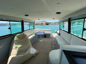 Interior view of a spacious boat cabin featuring comfortable seating and large windows, perfect for relaxing while enjoying scenic waterfront views.