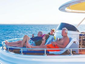 A group of friends relaxes on the deck of a yacht, enjoying drinks and the beautiful ocean view — perfect for a leisurely day on the water.
