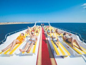 A lively group enjoys sunbathing on deck chairs aboard a boat, perfect for relaxation and fun on the water.