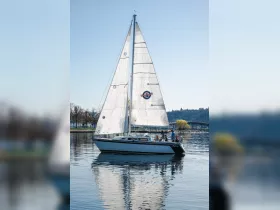 A group enjoys a sailing experience on a beautiful day, with the boat's reflection shimmering in the calm waters.
