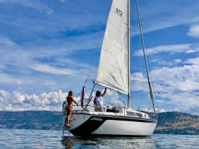 A couple enjoys a sunny day sailing on a beautiful lake, showcasing the joy of outdoor adventures on the water.