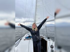 A joyful woman celebrates while sailing, arms wide open against a backdrop of cloudy skies and water — a perfect moment on the water.