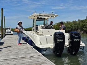 A woman stands by a boat at the dock while two men engage in conversation on board, showcasing a lively boating experience.