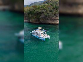 A lively group enjoys their time aboard the catamaran 'Margarita,' surrounded by stunning turquoise waters and lush greenery, perfect for a day of adventure.