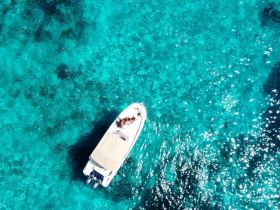 An aerial view of a boat surrounded by stunning turquoise waters, with guests enjoying their time on board — a perfect snapshot of a memorable day on the water.