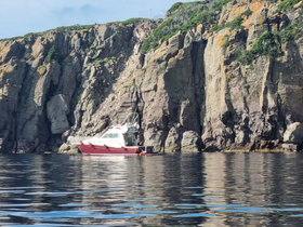 A serene view of a boat anchored near rugged cliffs, reflecting beautifully in the calm waters — an ideal setting for coastal exploration.