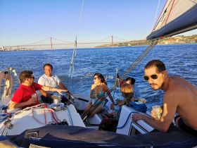 A lively group enjoys a sailing trip, sharing drinks and laughter against the backdrop of a stunning bridge — perfect for memorable outings on the water.