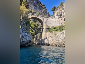 A stunning view of a historic bridge nestled between rocky cliffs, showcasing the breathtaking coastline — a perfect highlight for boat tours along scenic waterways.