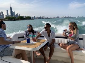 A lively group enjoys drinks aboard a boat with a stunning city skyline backdrop, perfect for a fun day on the water.