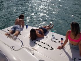A group of friends relaxes on the deck of a pontoon boat, enjoying drinks and soaking up the sun — the perfect setting for a fun day on the water.