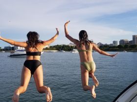 Two friends joyfully leap off the side of a boat into the water, capturing the essence of summer fun and adventure on the water.
