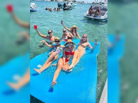 A fun group of friends enjoys a sunny day on a floating mat in clear waters, celebrating with drinks and laughter — the perfect summer getaway.