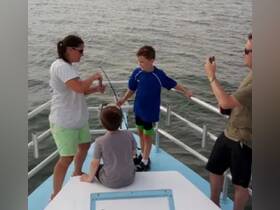 A family enjoys a fishing trip on a boat, with children engaged in the activity and capturing memories on camera — a perfect day on the water.