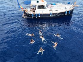 A lively group enjoys swimming in the deep blue sea, with a boat anchored nearby, creating the perfect backdrop for a fun day on the water.